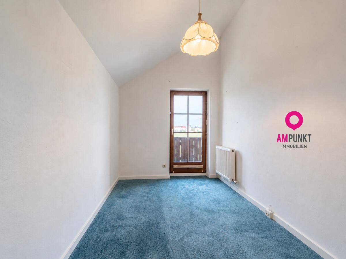 Schlafzimmer mit blauem Teppichboden, Dachschräge und Zugang zu einem französischen Balkon.