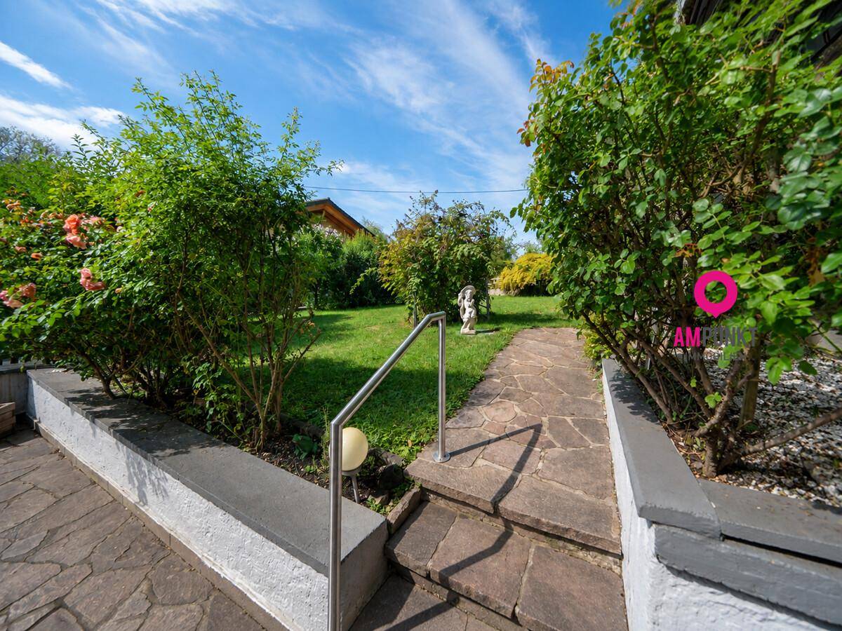 Gepflegter Gartenbereich mit Steinpfad, üppiger Bepflanzung und Rasenfläche.
