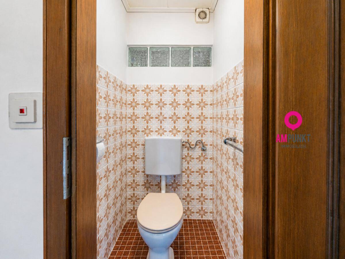 Kleines WC mit gemusterten Fliesen, WC und Haltegriff.