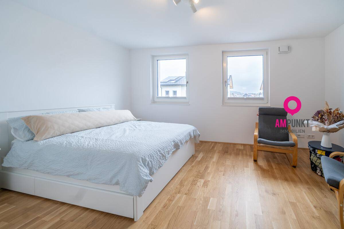 Helles Schlafzimmer mit Holzboden und zwei Fenstern.