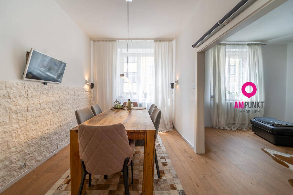 Moderner Essbereich mit Holztisch, strukturierter Wand und Fernseher, offen zum Wohnbereich.