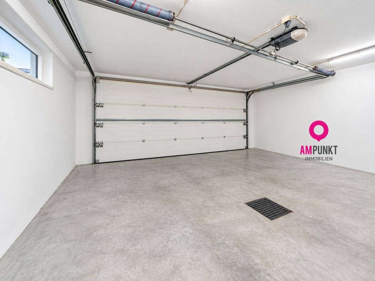 Geräumige Garage mit Betonboden, automatischem Tor und kleinem Fenster für Tageslicht.