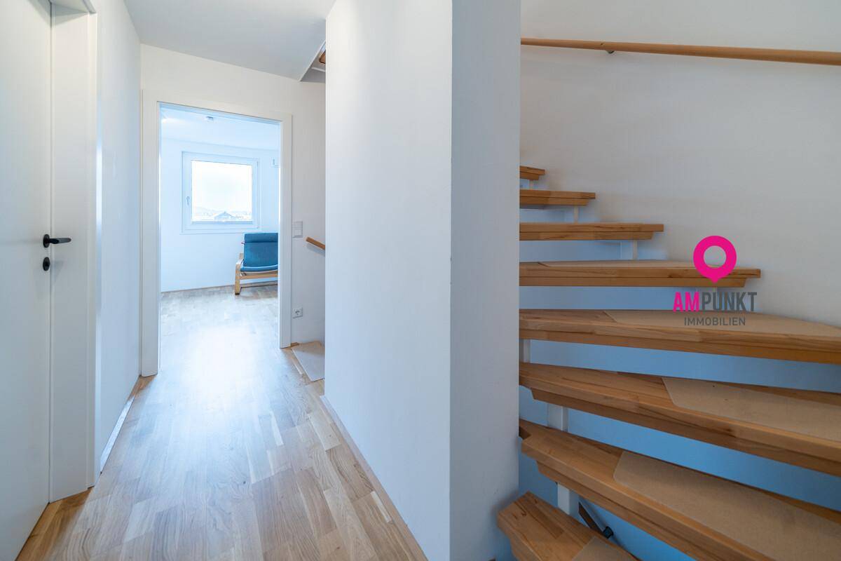 Heller Flur mit Holztreppe und Zugang zu weiteren Räumen.