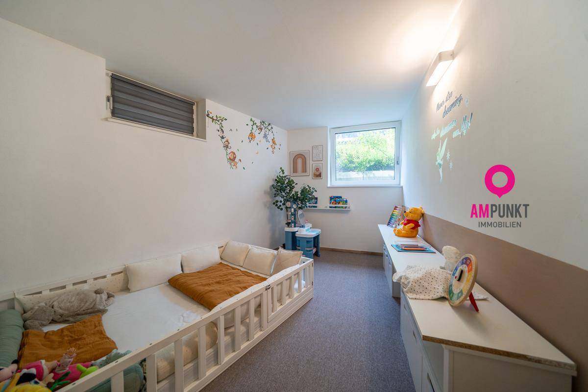Kinderzimmer mit hellem Fenster, Teppichboden und verspielter Wanddekoration.