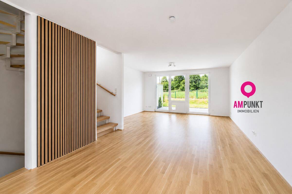 Geräumiger, leerer Wohn- und Essbereich mit Holzboden und großen Fenstern zum Garten.