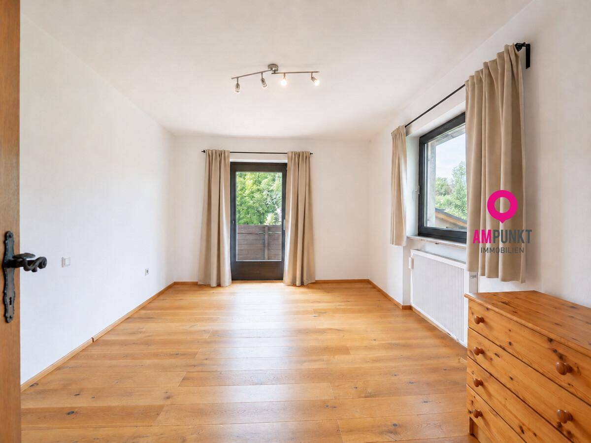 Helles Schlafzimmer mit Holzdielenboden und Zugang zu einem Balkon.