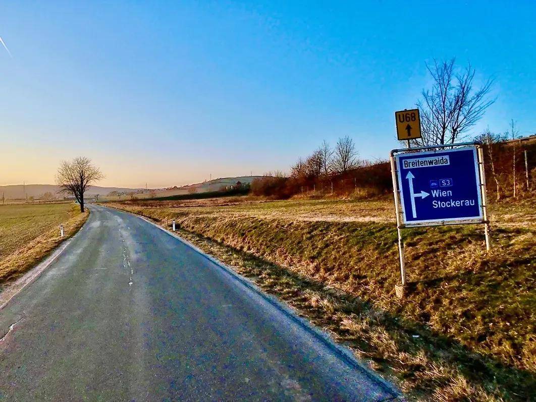 Ländliche Straße mit Wegweiser nach Breitenwaida, Wien und Stockerau bei Sonnenuntergang.