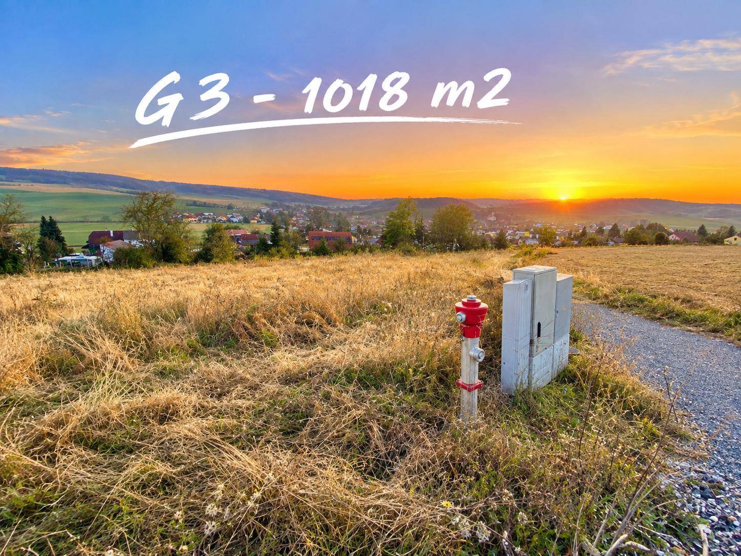 Baugrundstück G3 bei Sonnenuntergang mit Blick auf die umliegende Landschaft und ein Dorf.