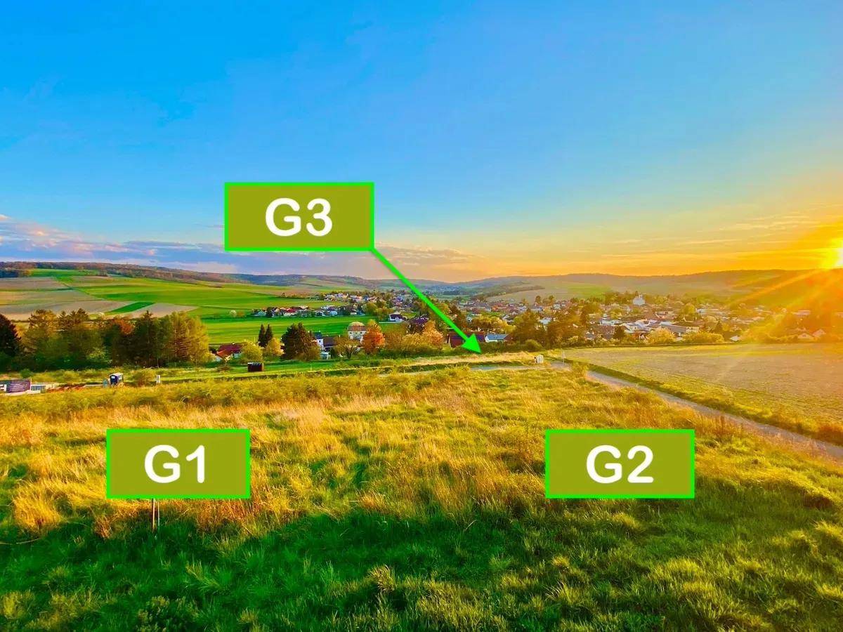 Luftaufnahme der Baugrundstücke G1, G2 und G3 mit Blick auf das Dorf und die grüne Umgebung bei Sonnenuntergang.