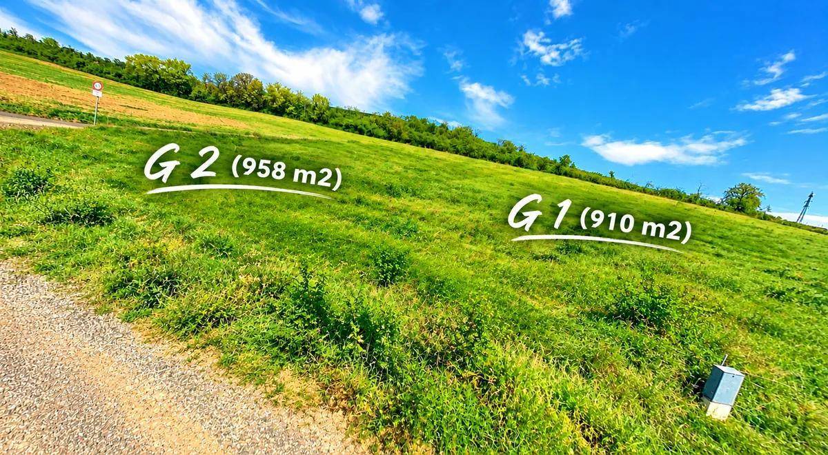Grüne Baugrundstücke G1 und G2 an einem Hang mit weitem Blick unter blauem Himmel.