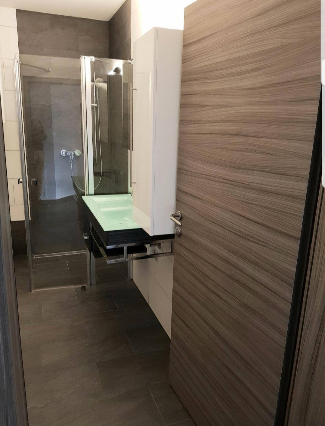Modernes Badezimmer mit Duschkabine und stilvollem Waschtisch mit grüner Glasplatte.