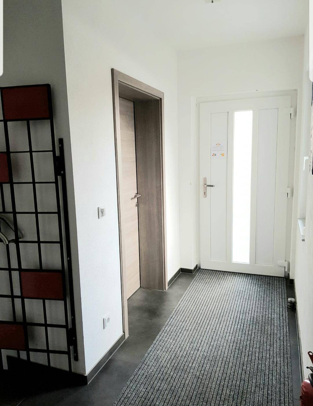 Heller Eingangsbereich mit moderner weißer Haustür, Holztüren und dunklem Fliesenboden.