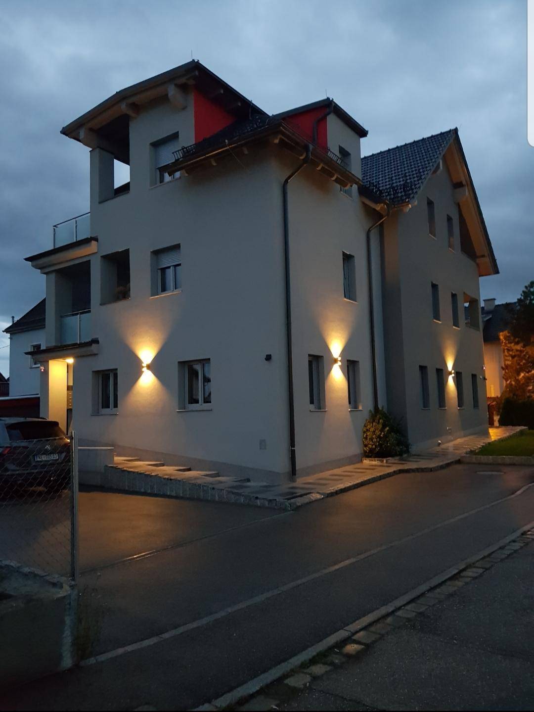 Das moderne Gebäude bei Dämmerung mit stilvoller Außenbeleuchtung und barrierefreiem Zugang über eine Rampe.