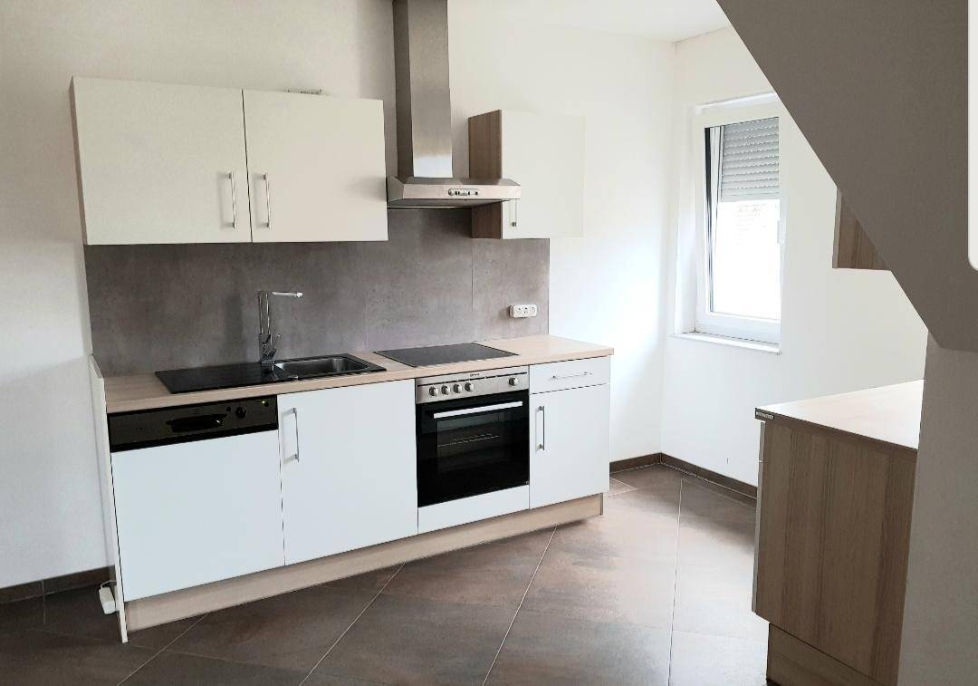 Funktionale Küche mit weißen Schränken, Backofen, Geschirrspüler und Dunstabzugshaube.