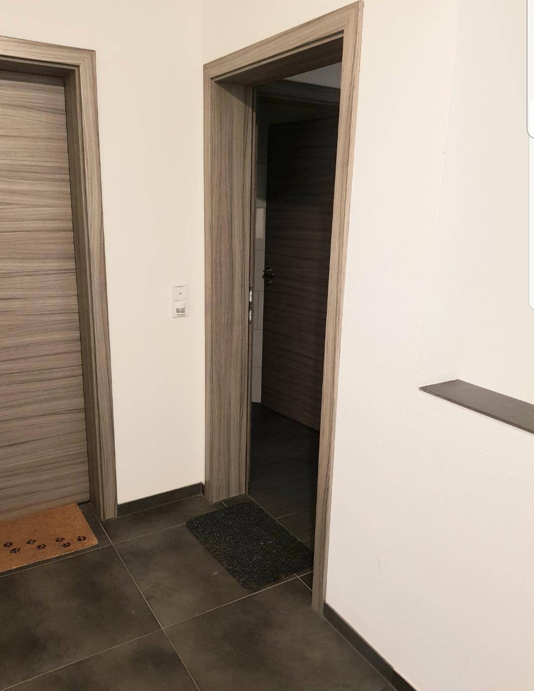 Flur mit zwei modernen Holztüren und dunklem Fliesenboden, der zu weiteren Räumen führt.