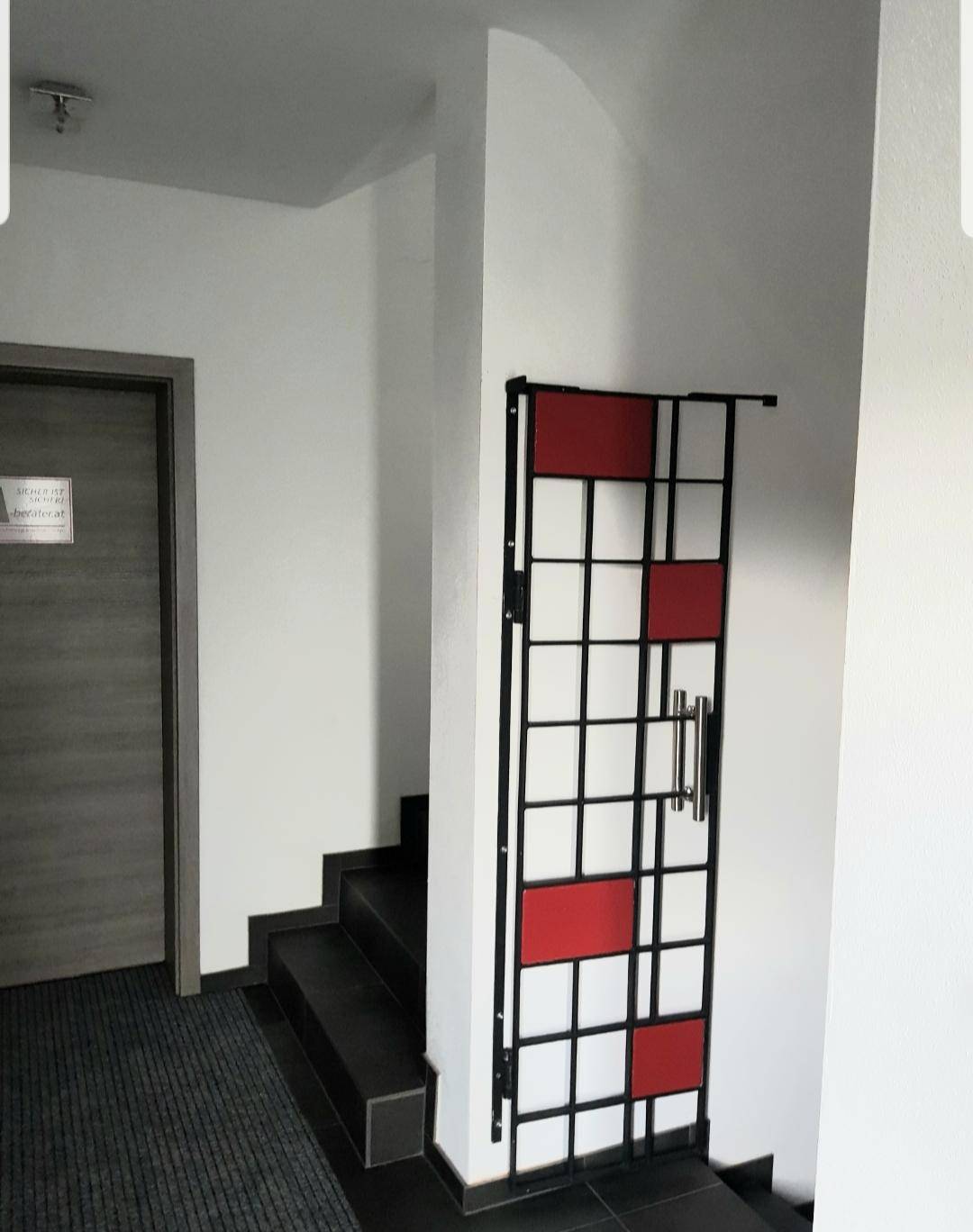 Heller Flur mit einer modernen, rot-schwarzen Metalltür und einer schlichten Holztür.