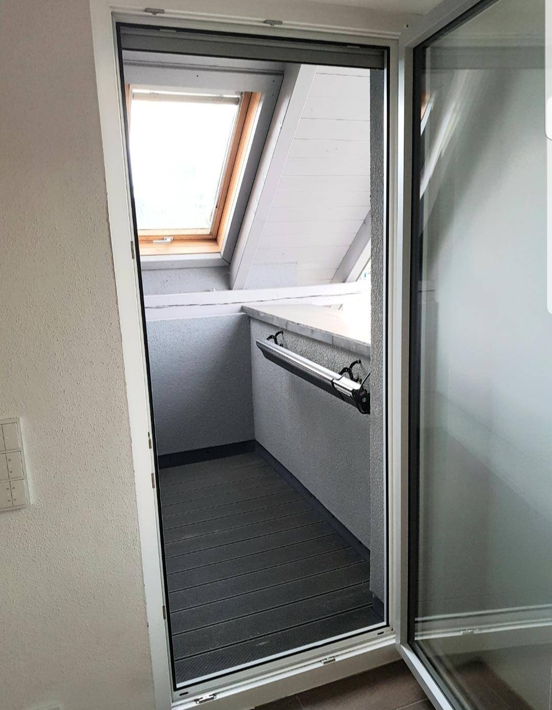 Kleiner Balkon mit Holzdielenboden und einem Dachfenster, das viel Licht spendet.