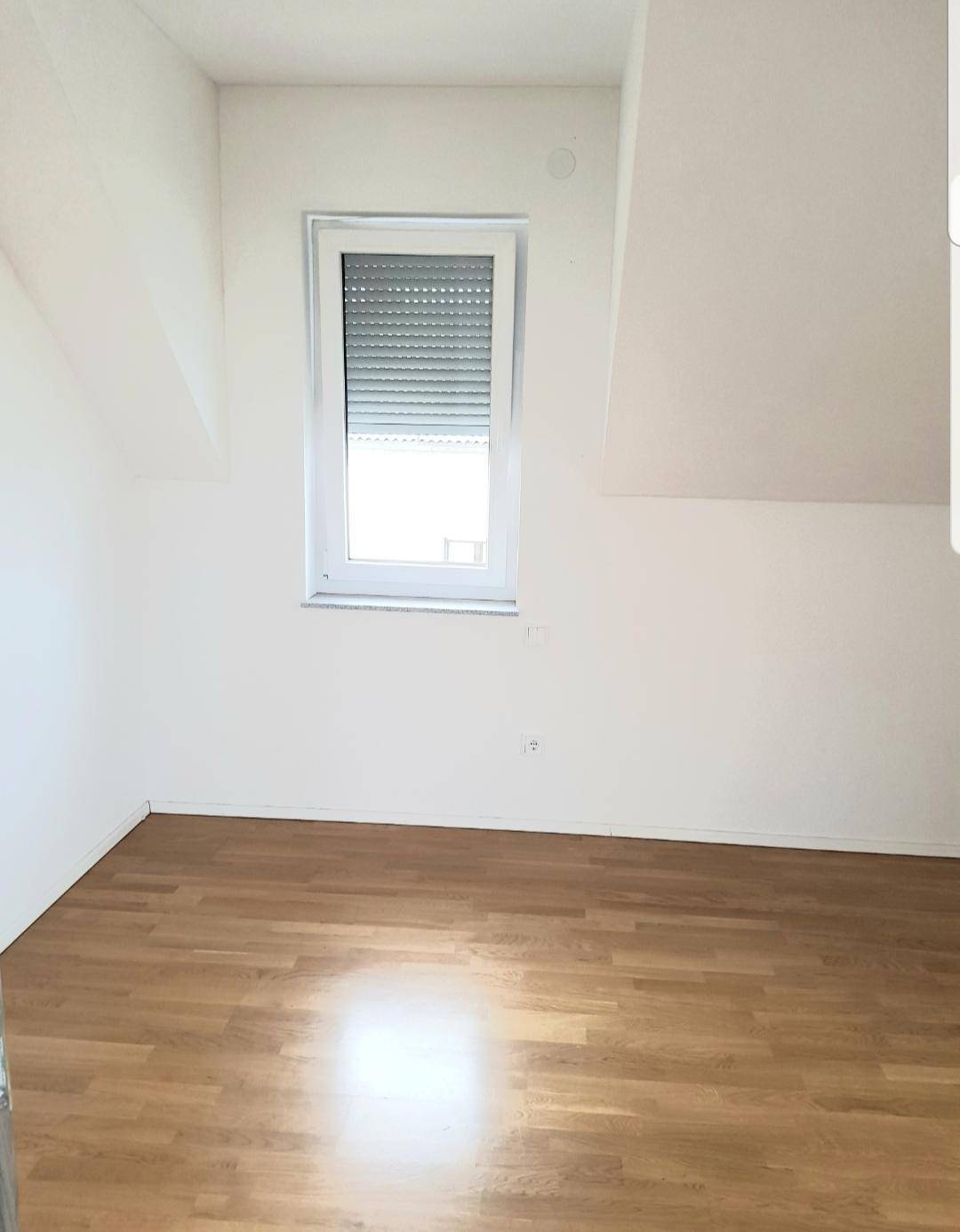 Gemütliches Schlafzimmer mit Holzboden, Fenster mit Rollladen und Dachschräge.