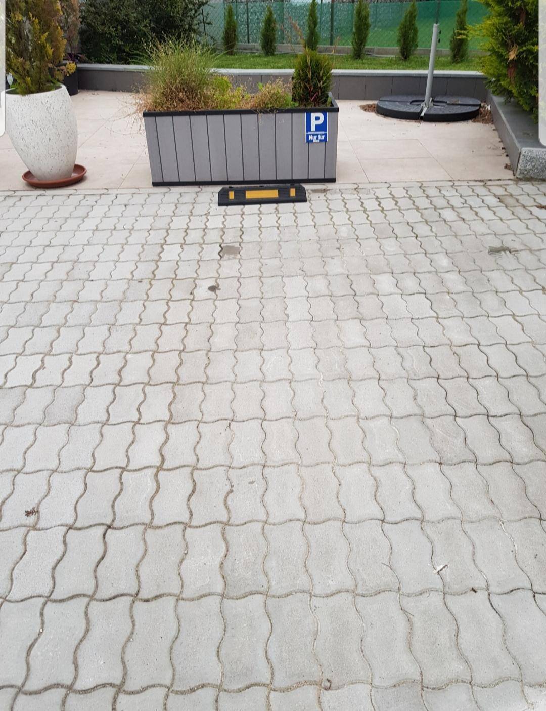 Gepflasterter Außenparkplatz mit einem markierten Stellplatz für Fahrzeuge.