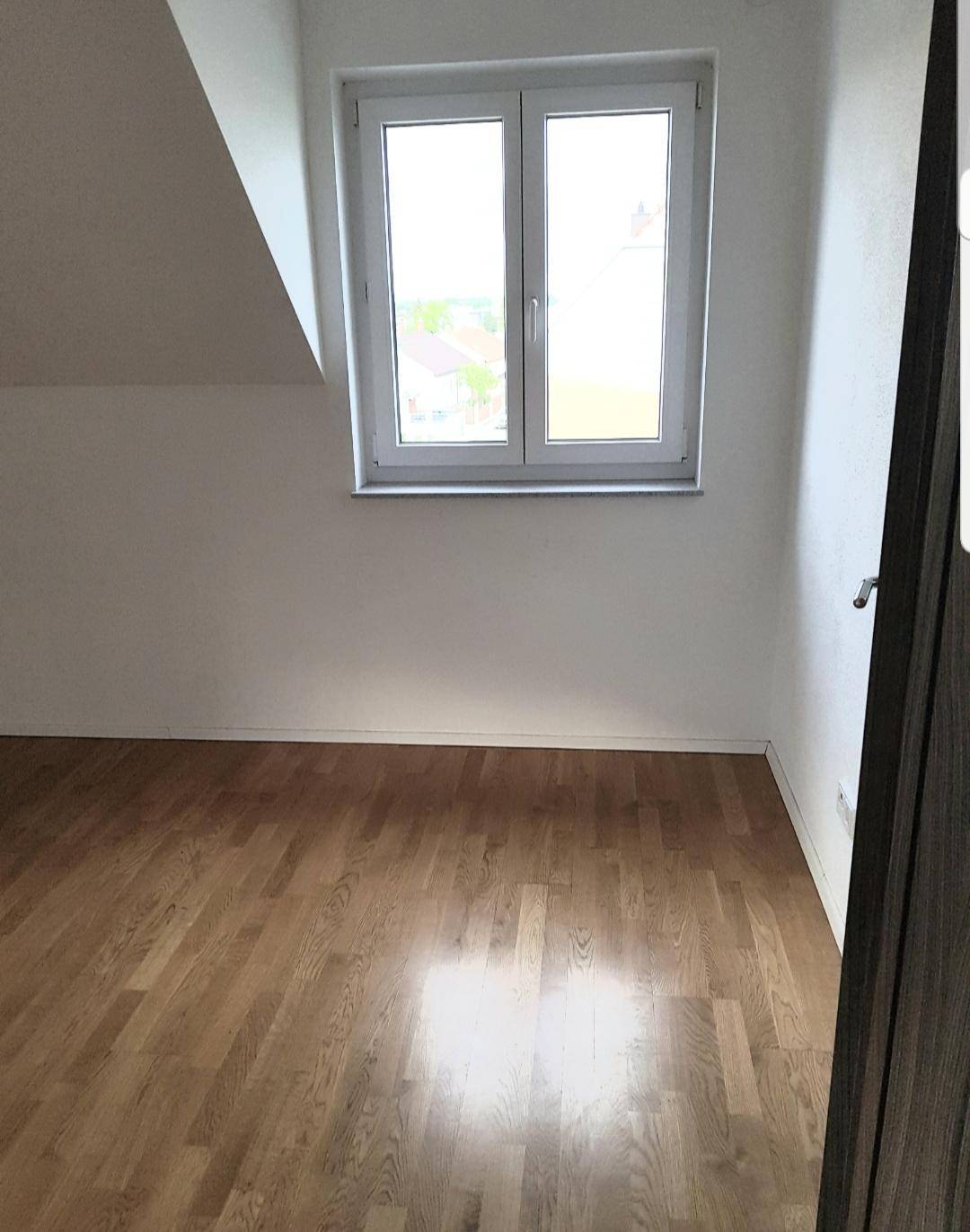Helles Schlafzimmer mit Holzboden und Fenster, unter einer leichten Dachschräge gelegen.