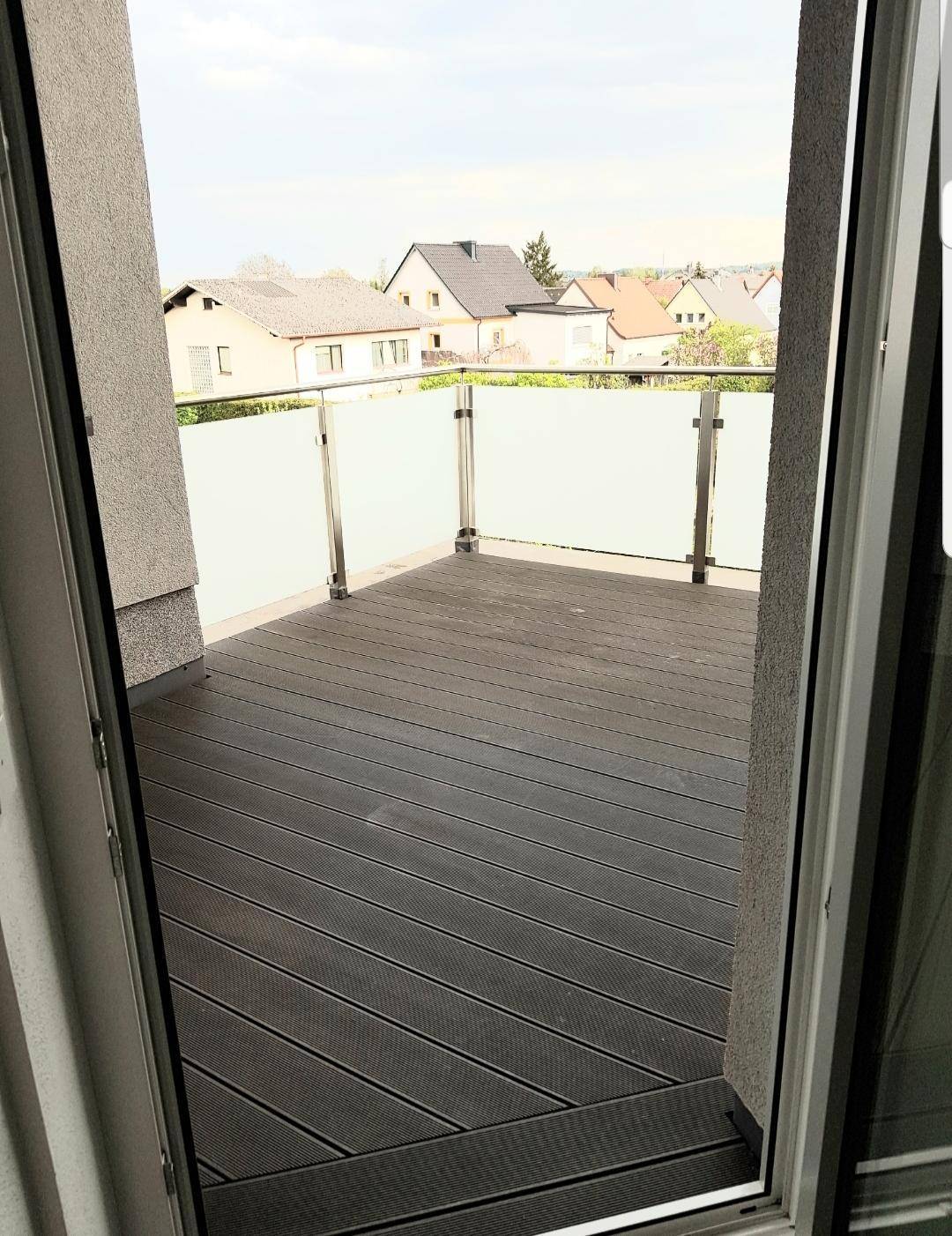 Geräumiger Balkon mit Holzdielenboden und Glasgeländer, bietet einen Blick auf die Umgebung.