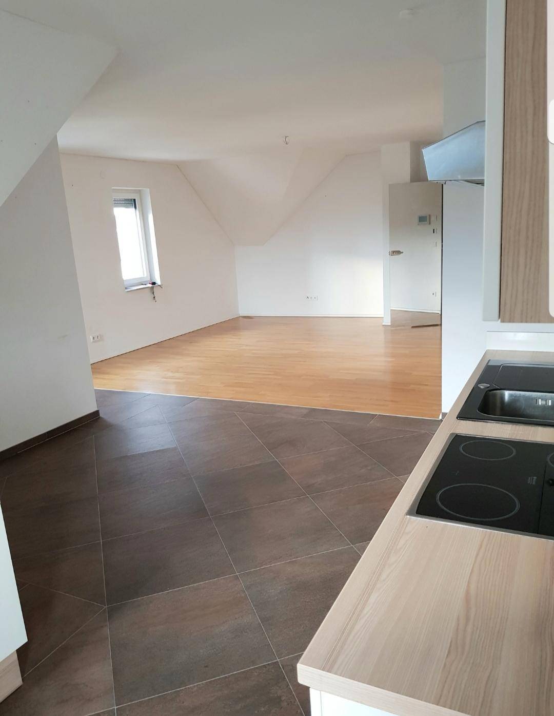 Heller Wohn- und Küchenbereich mit Holzboden, Kochfeld und Dachschrägen.