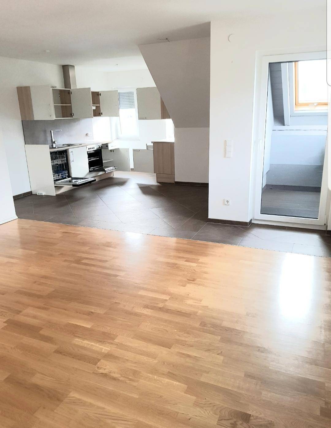 Offener Wohnbereich mit Holzboden und integrierter Küche im Hintergrund unter Dachschrägen.