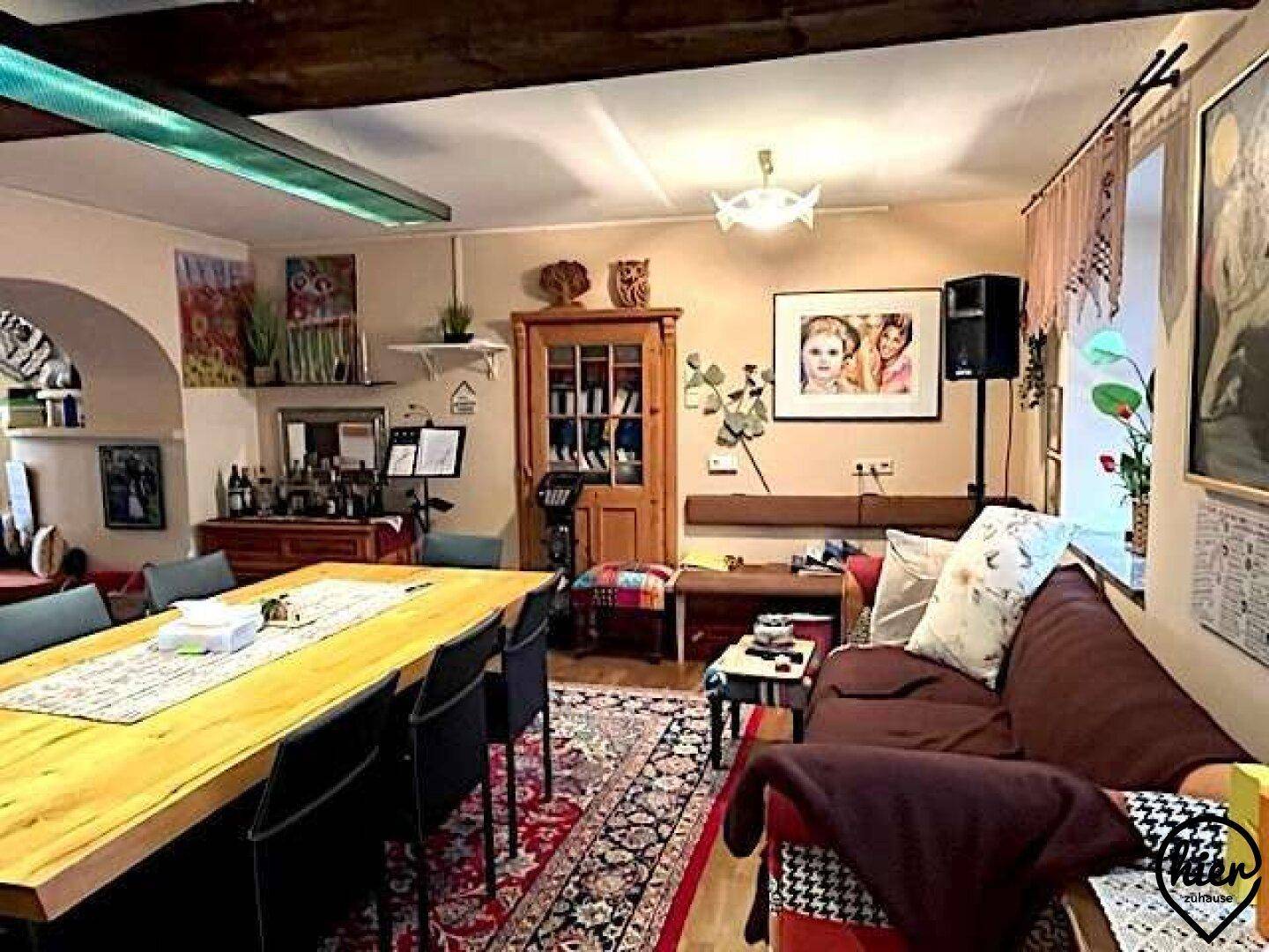 Gemütlicher Wohn-Essbereich mit großem Holztisch, Sofa und Teppichen, ideal für gesellige Runden.