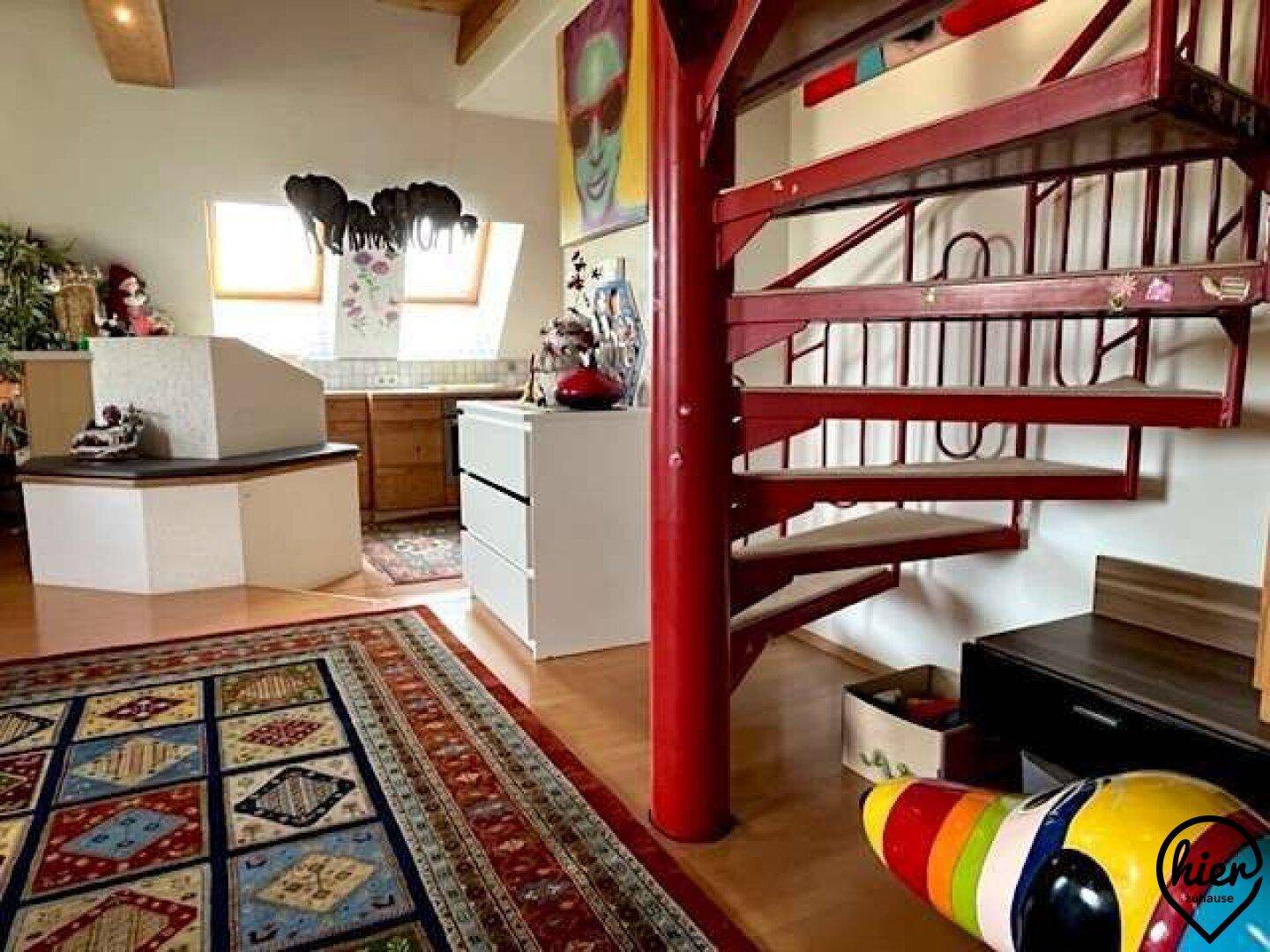 Heller Wohnbereich mit auffälliger roter Wendeltreppe, farbenfrohem Teppich und moderner Kunst.