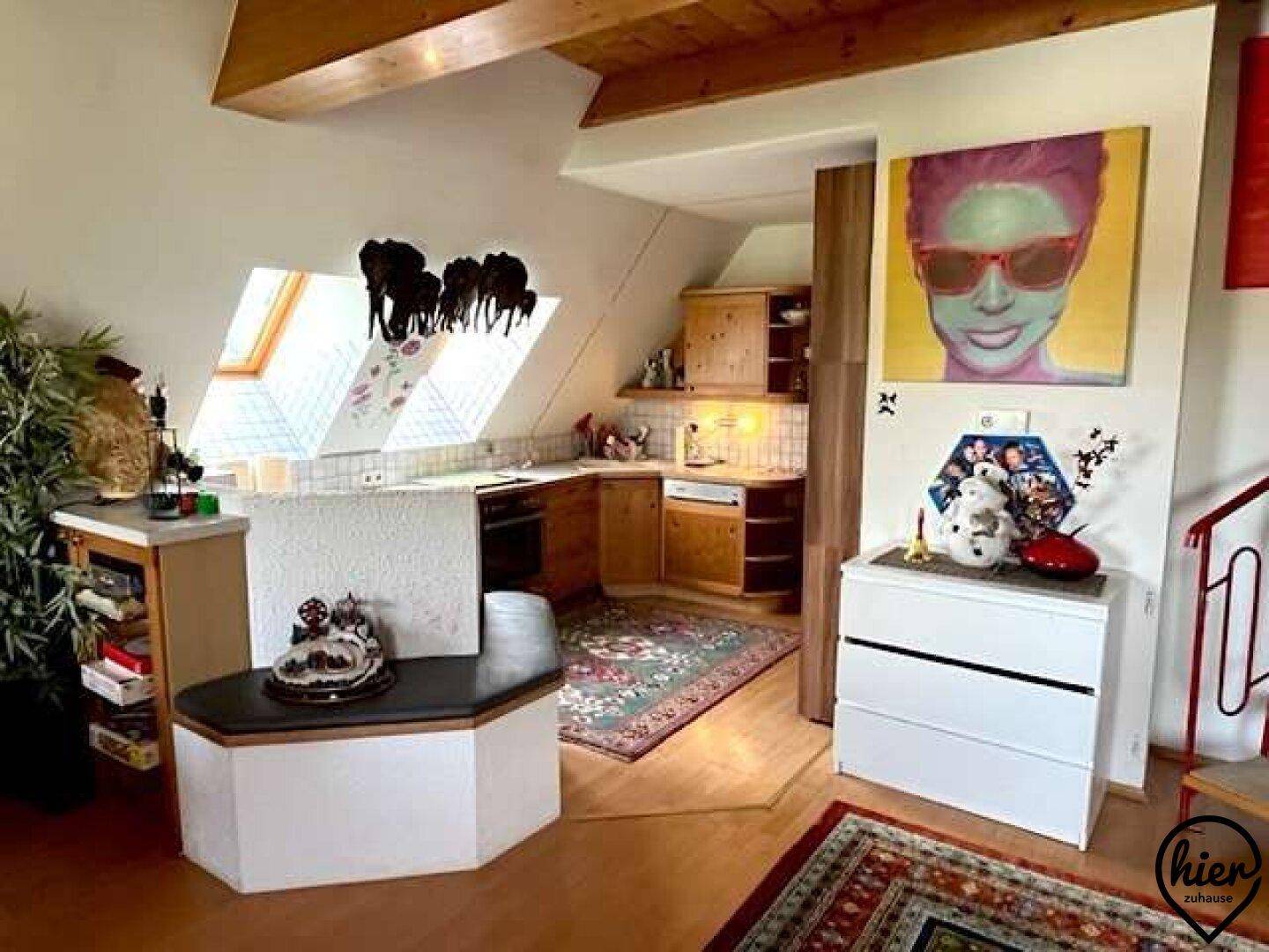 Offene Küche im Dachgeschoss mit Holzschränken, Dachfenstern und farbenfroher Kunst an der Wand.