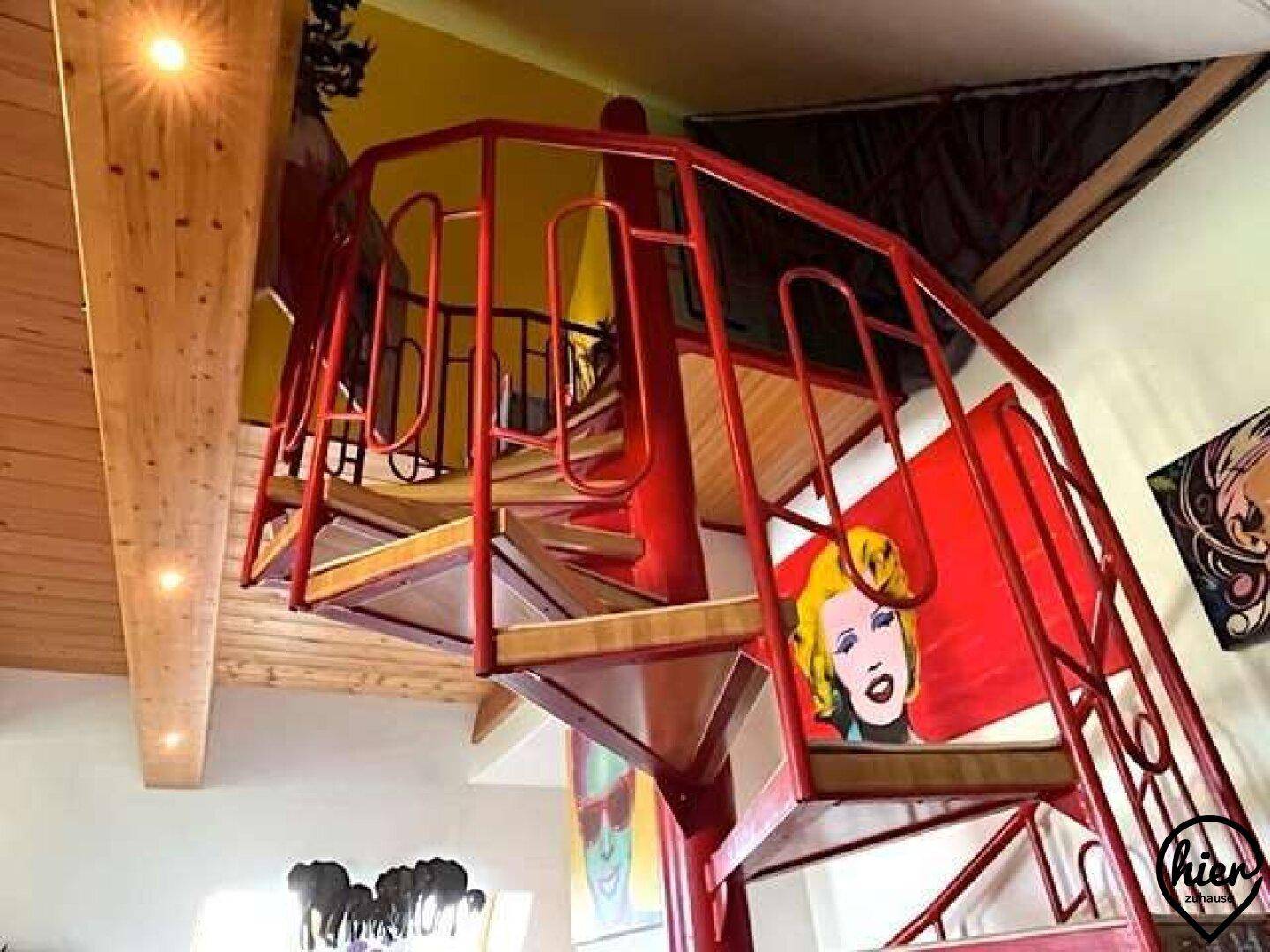Auffällige rote Wendeltreppe mit Holzdecke und Pop-Art-Gemälden, die die Etagen verbindet.