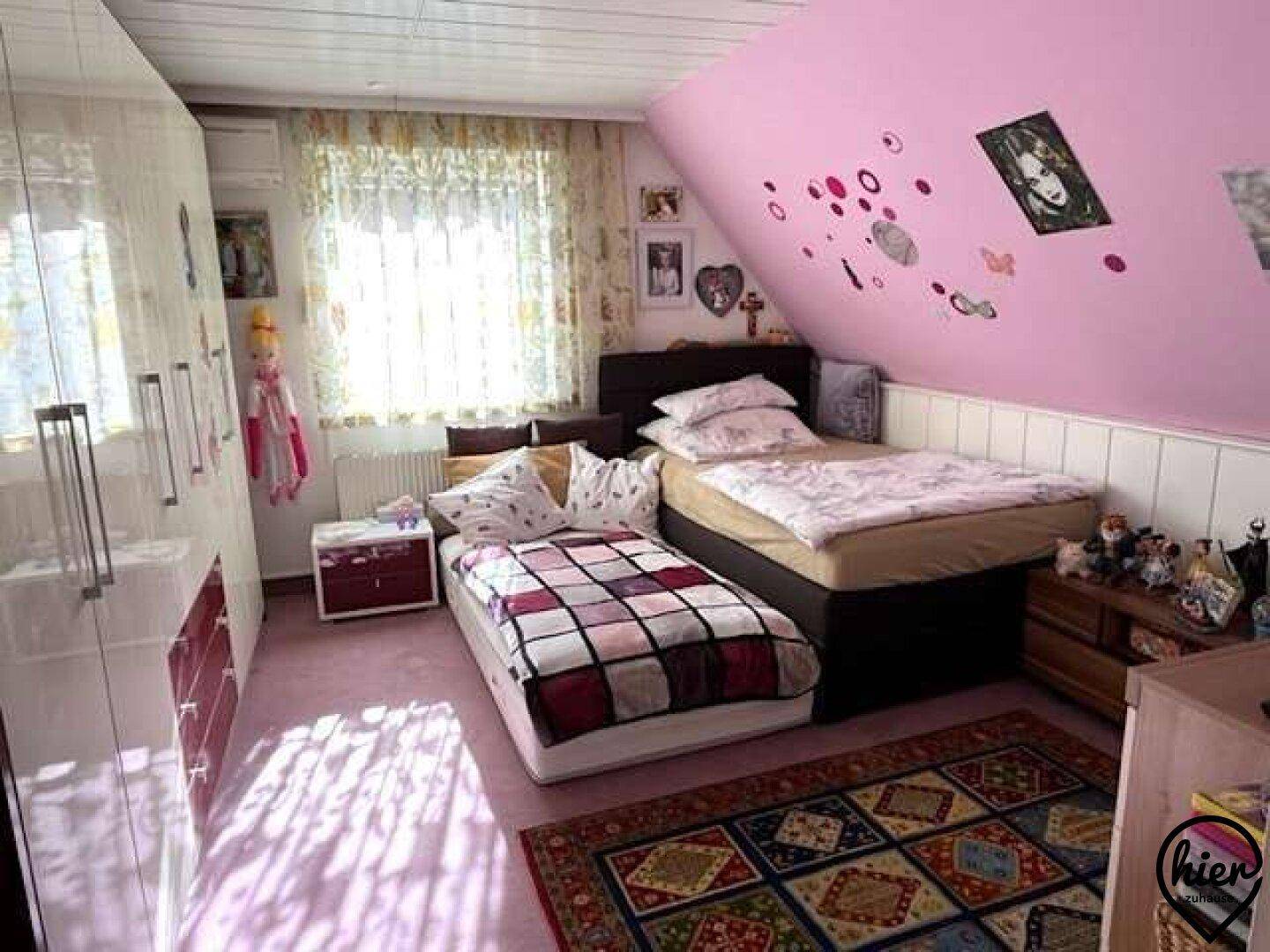 Helles Schlafzimmer im Dachgeschoss mit rosa Wänden, zwei Betten und einem großen Kleiderschrank.