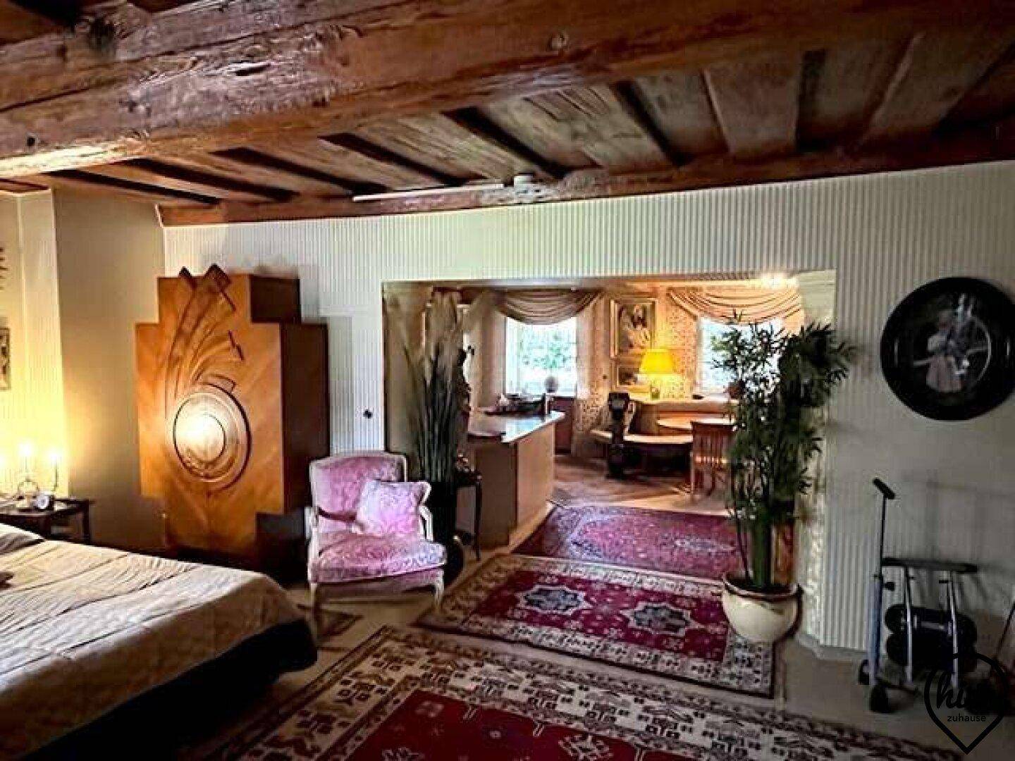 Wohnzimmer mit Holzbalken, einem Bett und Blick auf den angrenzenden Essbereich mit Fenster.