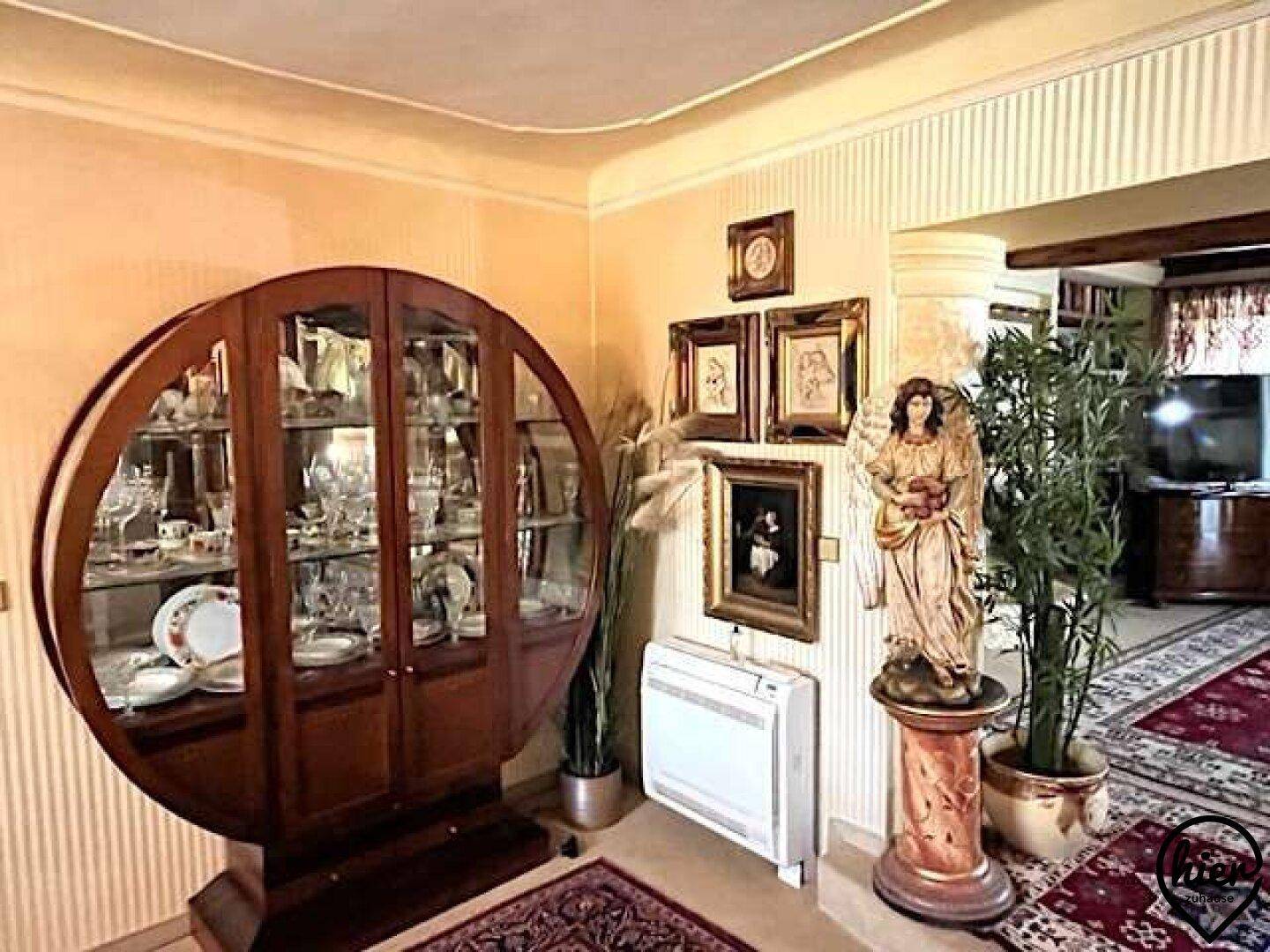 Geräumiger Flur mit großer Vitrine, klassischer Statue und Pflanzen, geschmückt mit traditionellen Teppichen.