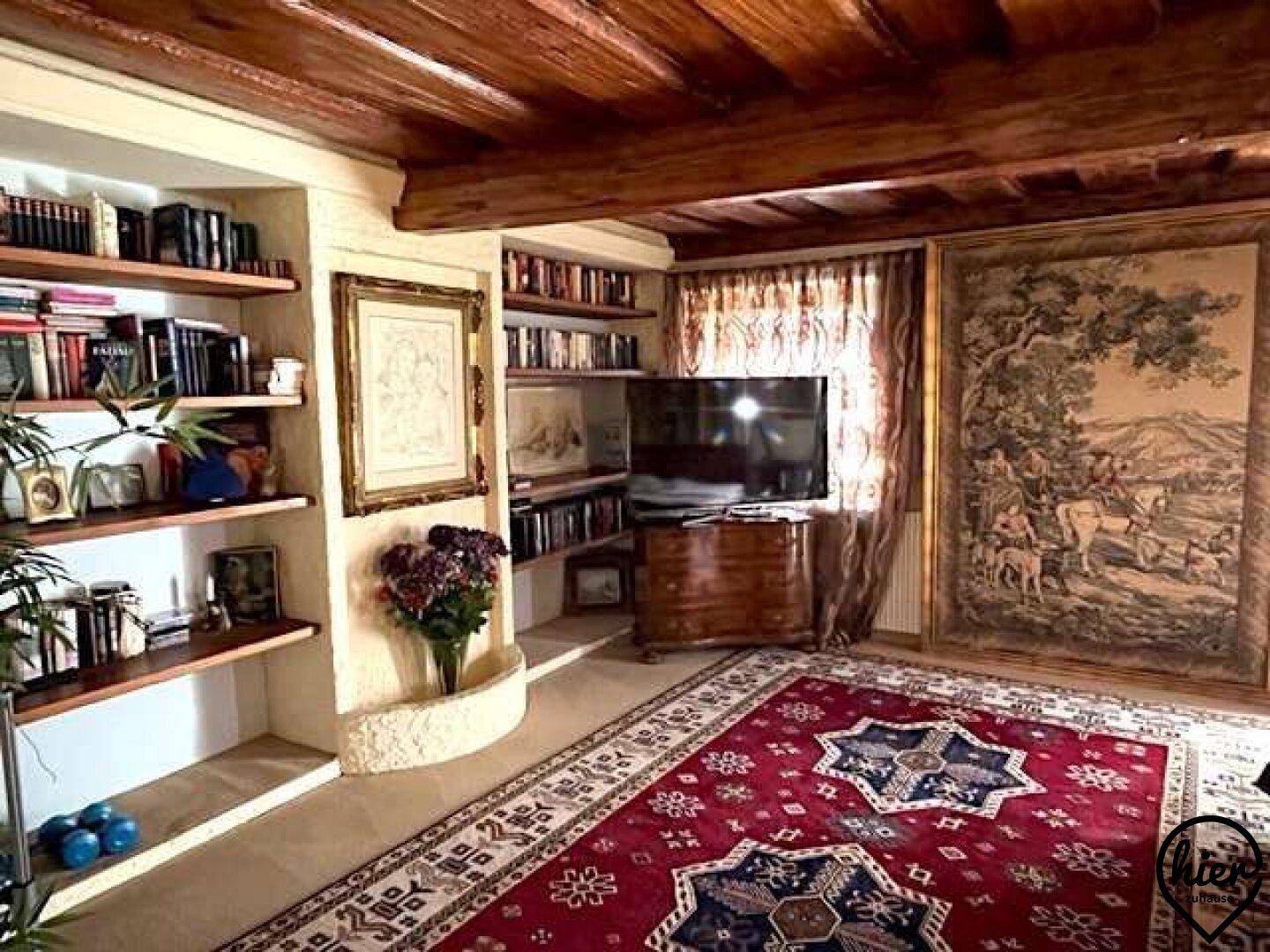 Wohnzimmer mit rustikalen Holzbalken, eingebauten Bücherregalen und einem großen Wandteppich.