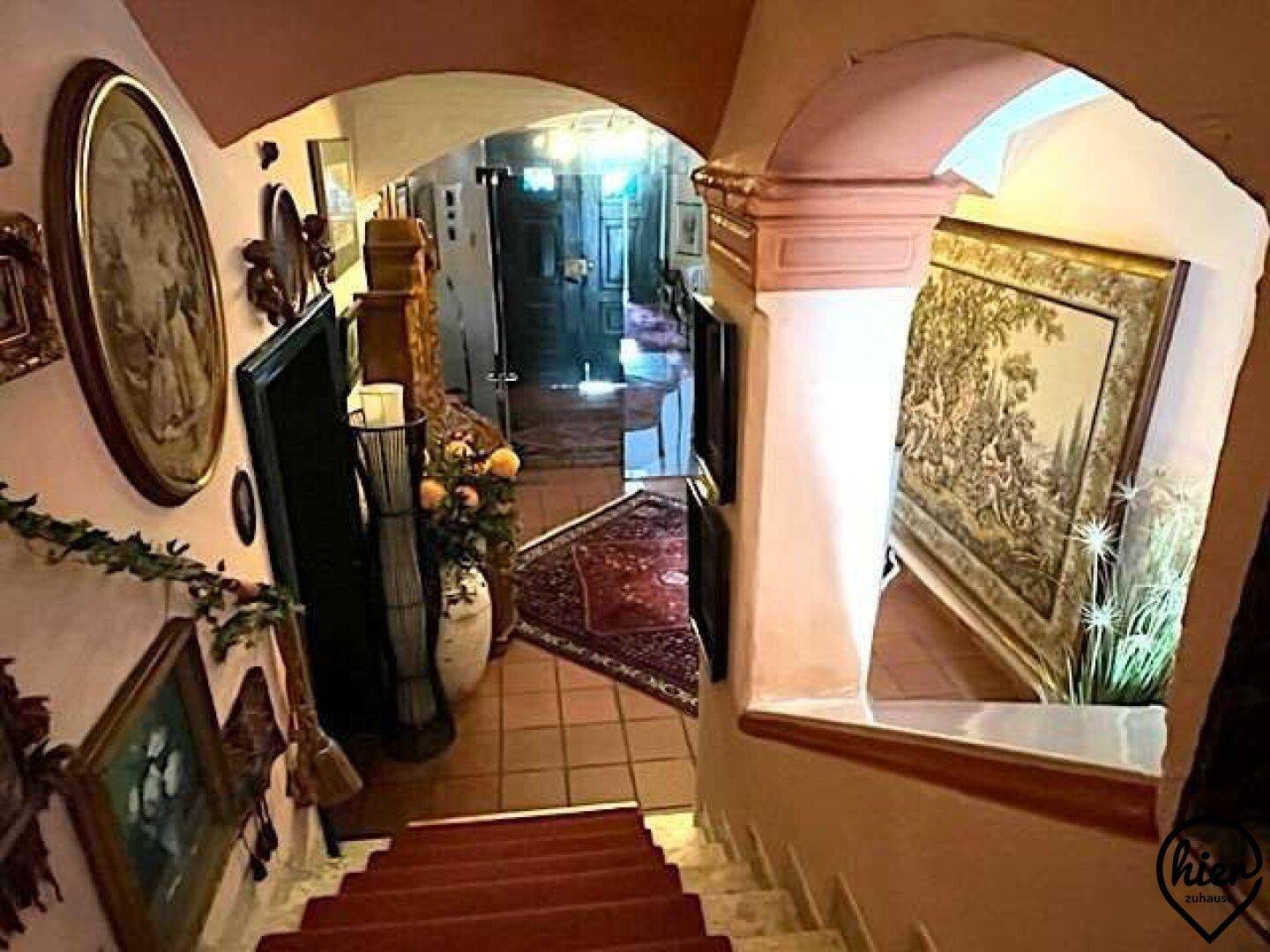 Treppenabgang mit Fliesenboden, kunstvollen Gemälden und Blick auf den Eingangsbereich.