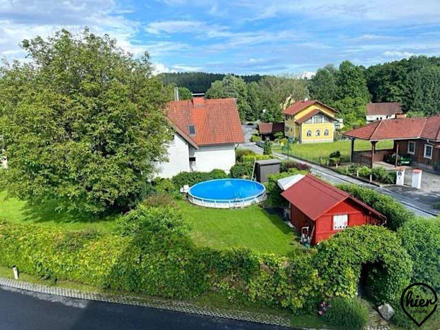 Blick von oben auf einen Garten mit Rasenfläche, Bäumen und einem Aufstellpool in einer Wohnsiedlung.