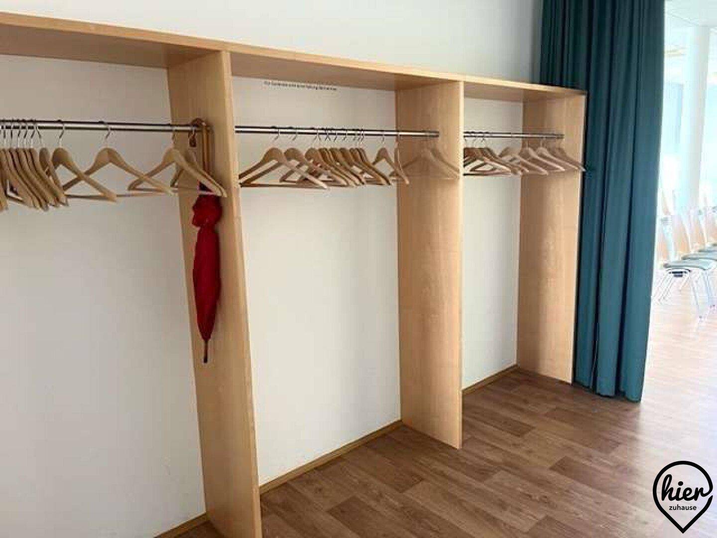 Garderobenbereich mit Holzelementen, Kleiderstangen und Vorhängen in einem Veranstaltungsraum.