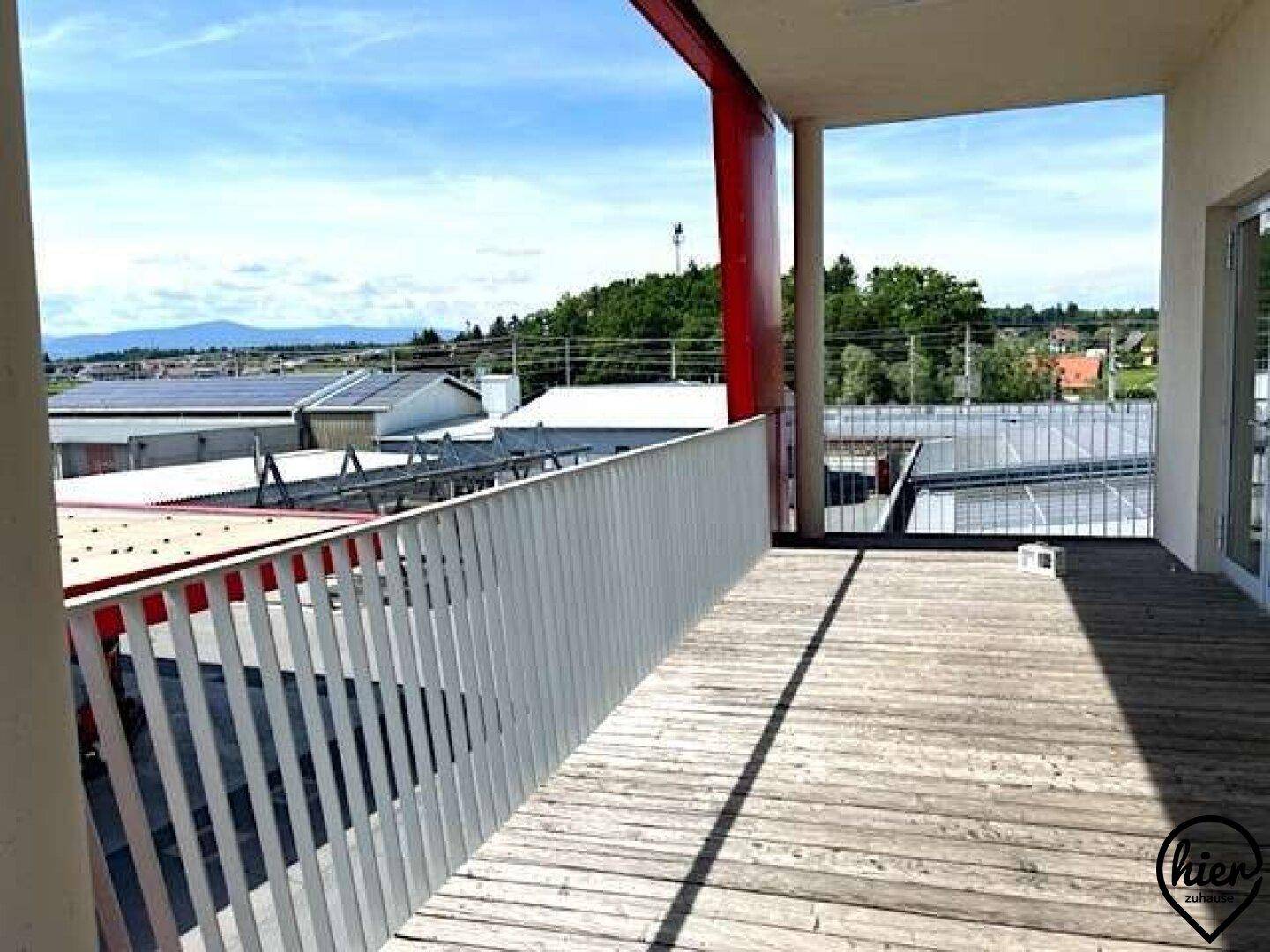 Holzterrasse mit Blick auf umliegende Gebäude, Dächer und die weite Landschaft.