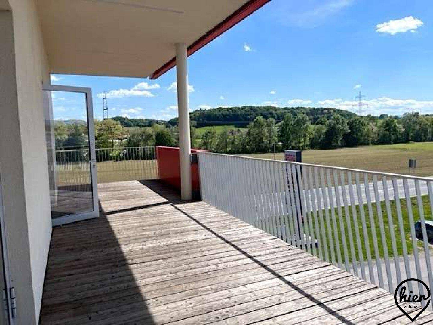 Große Holzterrasse mit weißem Geländer und weitem Blick auf die grüne Landschaft.