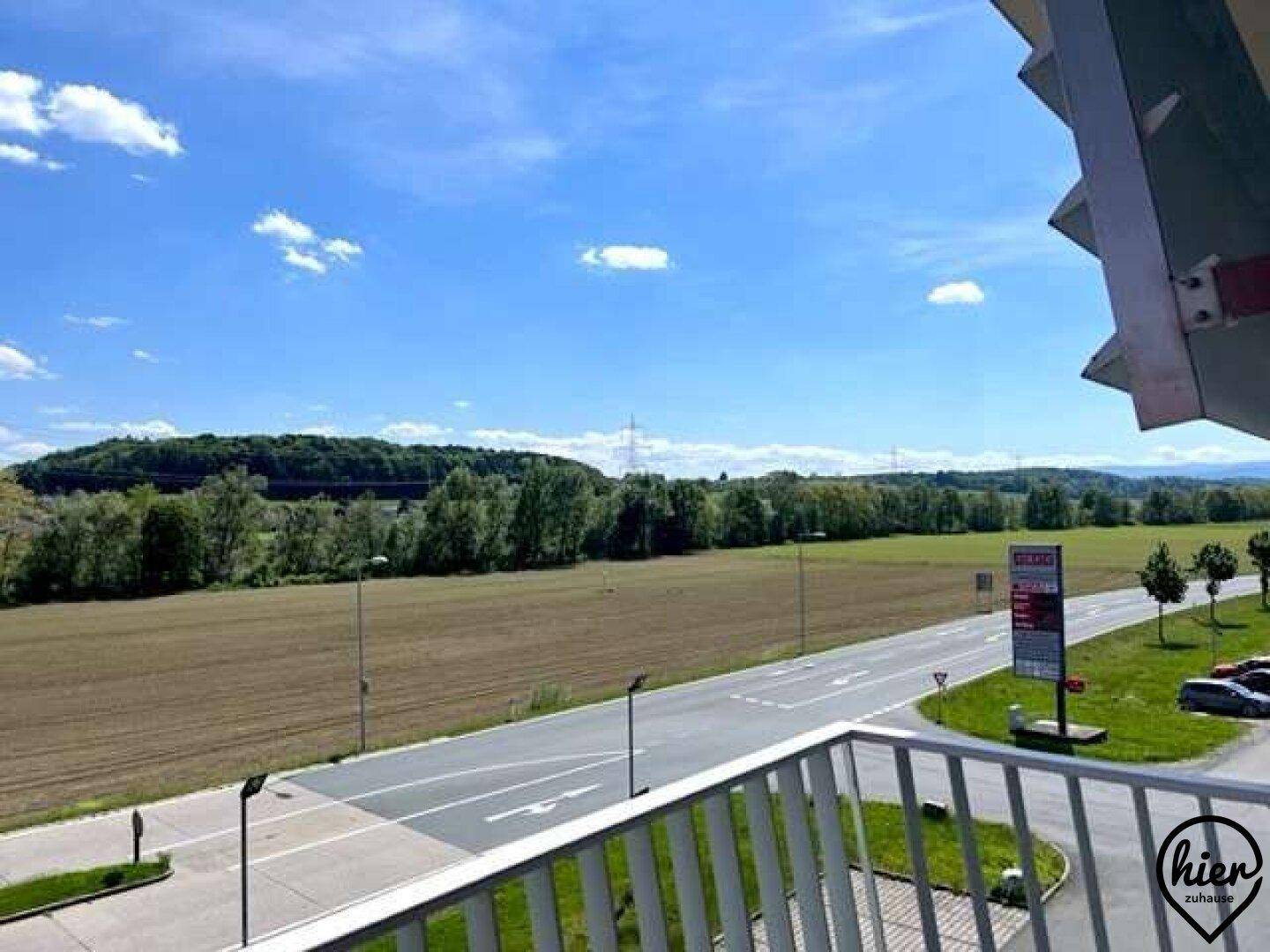 Terrasse mit weitem Blick über eine Straße, Felder und bewaldete Hügel.