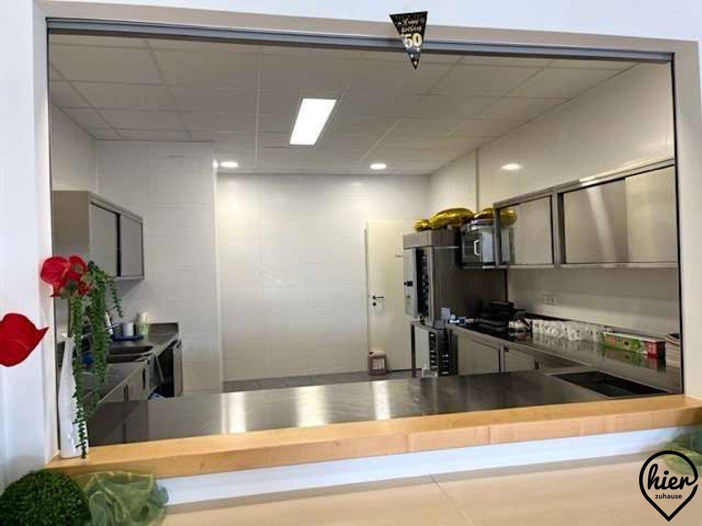 Professionelle Cateringküche mit Edelstahloberflächen und einem Durchgang zum Veranstaltungsraum.