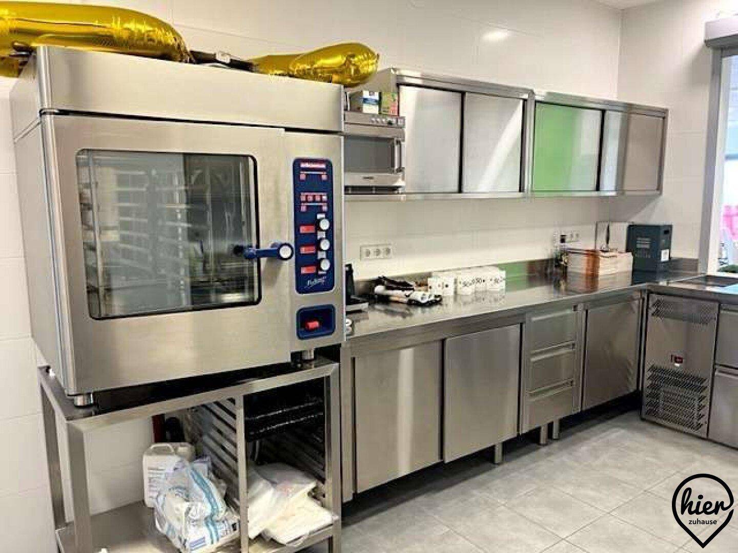 Professionelle Cateringküche mit großem Konvektomaten, Edelstahlschränken und Arbeitsflächen.