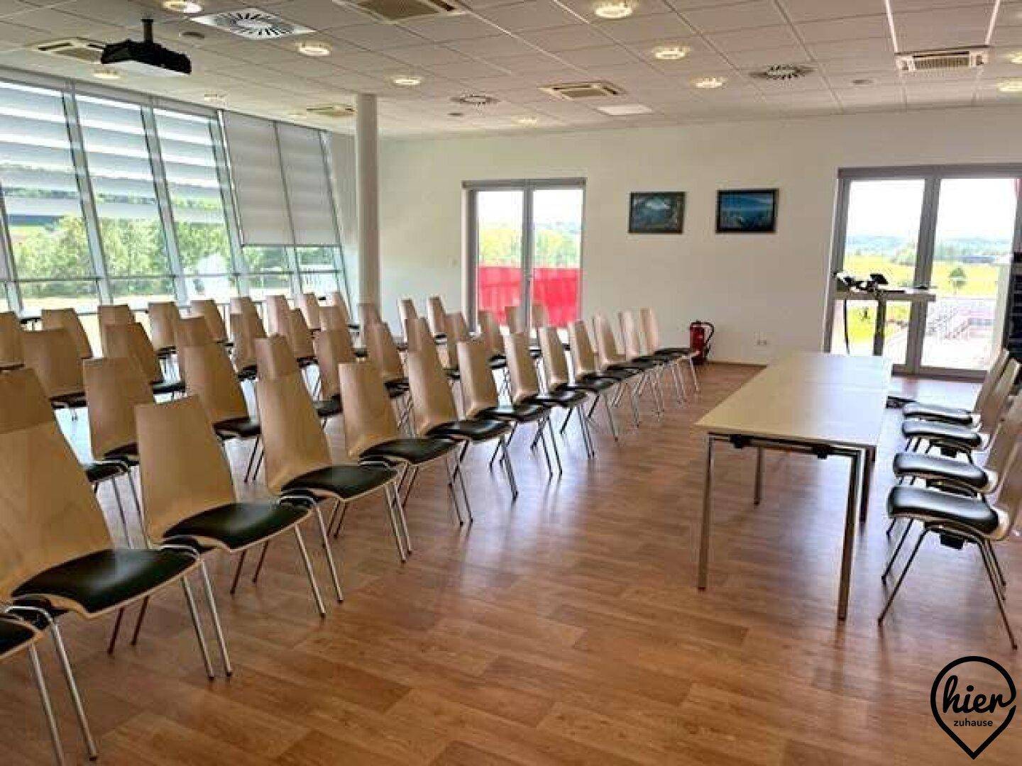 Großer Konferenzraum mit Reihenbestuhlung, Holzboden und weitem Blick ins Grüne.