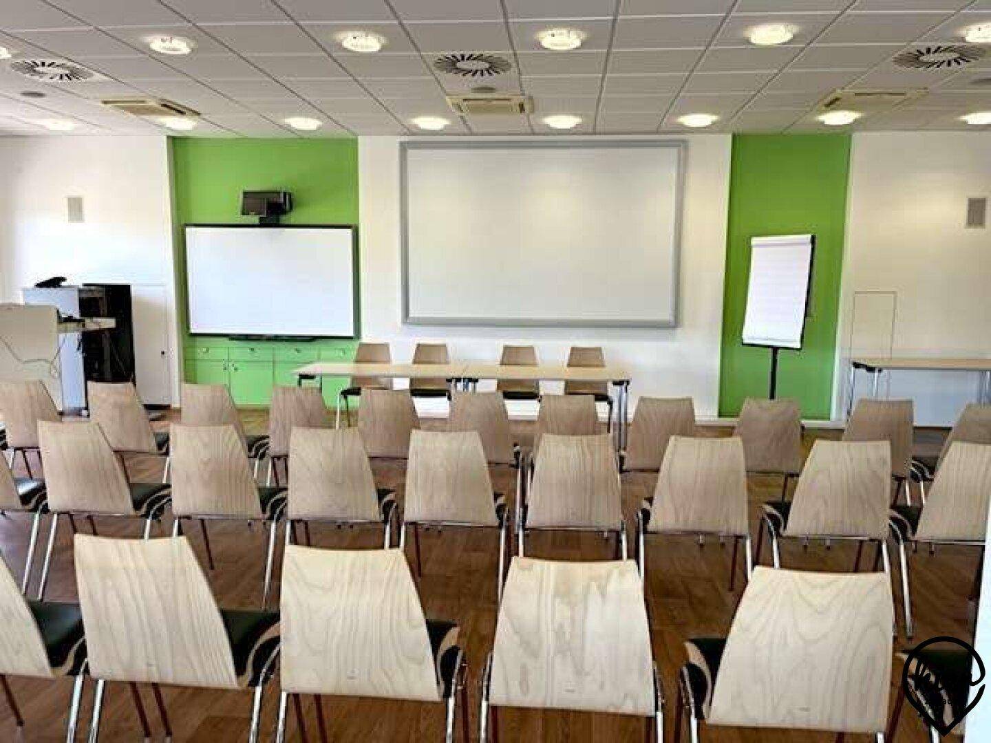 Konferenzraum mit Reihenbestuhlung, Projektionsflächen und grünen Akzentwänden.