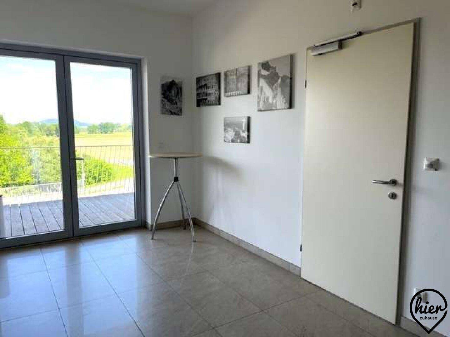 Heller Innenraum mit Fliesenboden, einer Tür und großen Glastüren, die zu einem Balkon mit Weitblick führen.