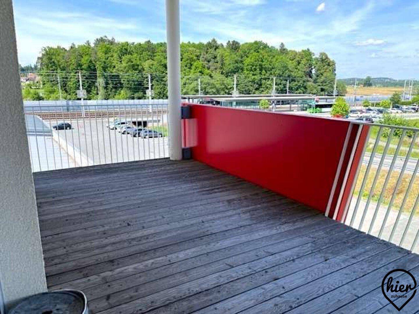 Balkonbereich mit Holzboden, weißen Geländern und einem markanten roten Designelement.