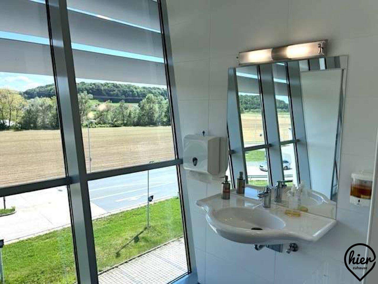 Badezimmer mit Waschbecken, Spiegel und großen Fenstern, die einen weiten Blick auf die Landschaft bieten.
