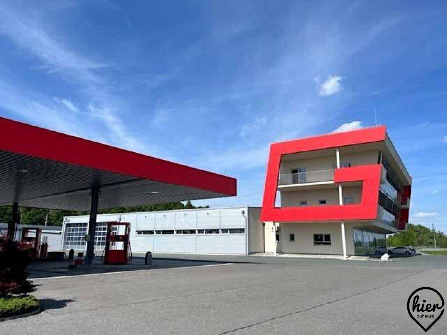Modernes Gebäude mit markanten roten Architekturelementen neben einer Tankstelle.
