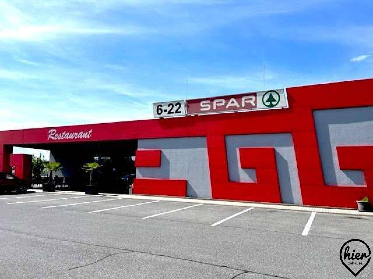 Gewerbegebäude mit "SPAR"- und "Restaurant"-Beschilderung, gekennzeichnet durch rote und graue Fassadenelemente.